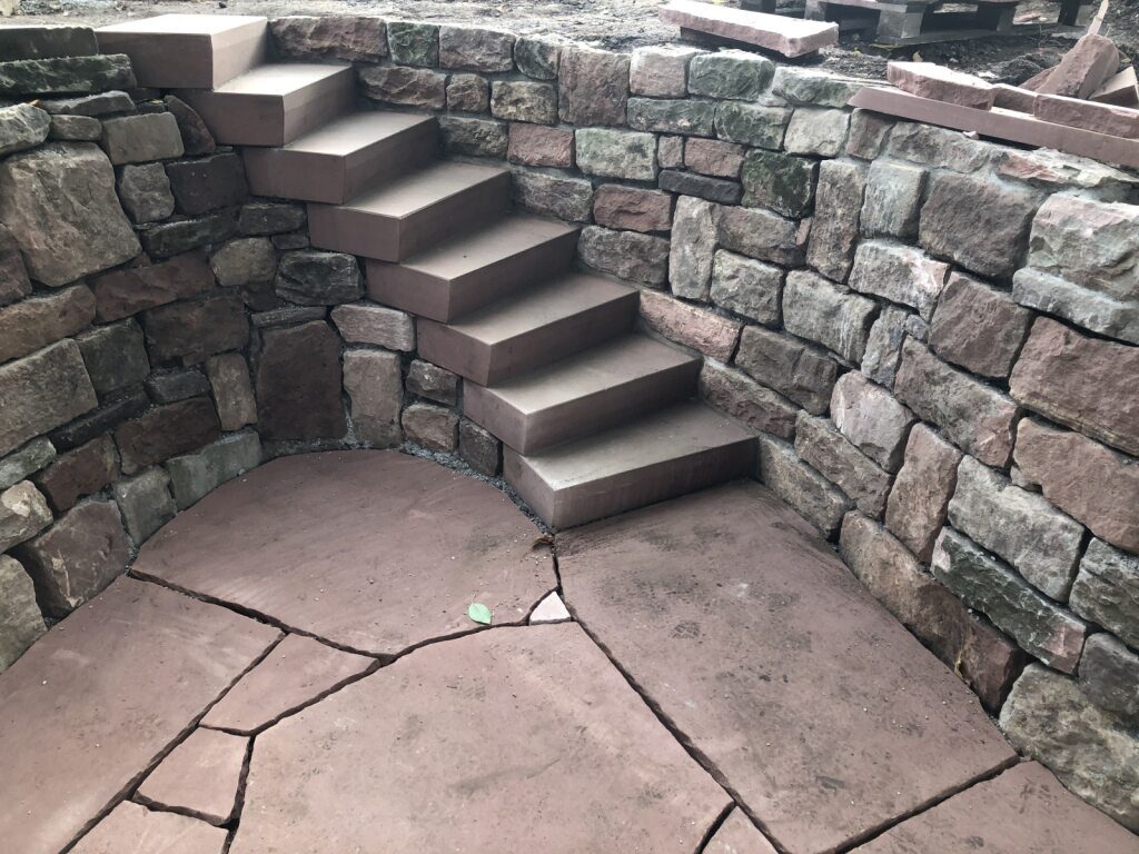 You see a curved natural stone wall made of sandstone with a spiral staircase built into it.